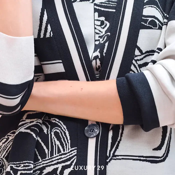 Close-up of a person wearing a black and white patterned cardigan with visible branding.